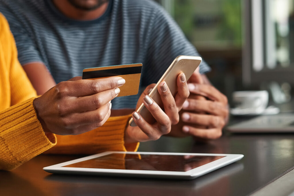 Close-up of a woman sitting with his friend in cafe holding credit card and mobile phone for shopping online