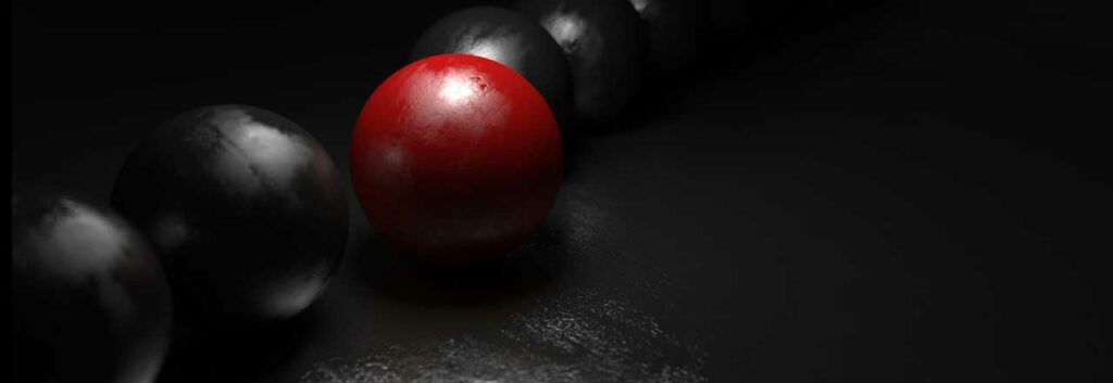 Photo of a red ball in a row of black balls in a dimly lit space.