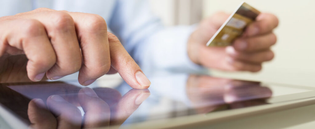 Closeup photo of a man using a tablet while holding a credit card.