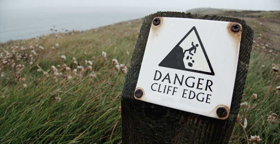 Photo of a sign on a wood post which reads "Danger: cliff edge".