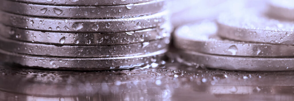 A closeup photograph of coins covered in beads of water.
